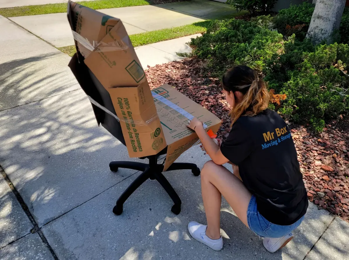 A Mr. Box mover taping cardboard around an office chair
