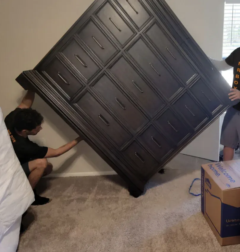 Two movers tilting a large dark dresser in a bedroom