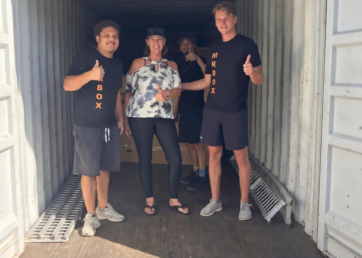 A customer and three movers posing among boxes inside a storage container