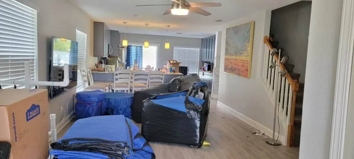 Wrapped living-room furniture and folded blankets beside a staircase