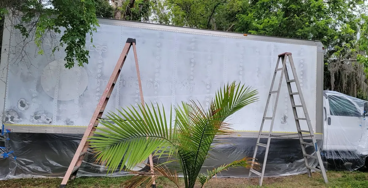 A moving truck masked for painting with two ladders beside it
