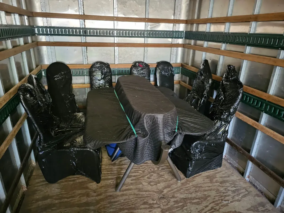 Individually wrapped dining chairs surrounding padded table pieces inside a truck