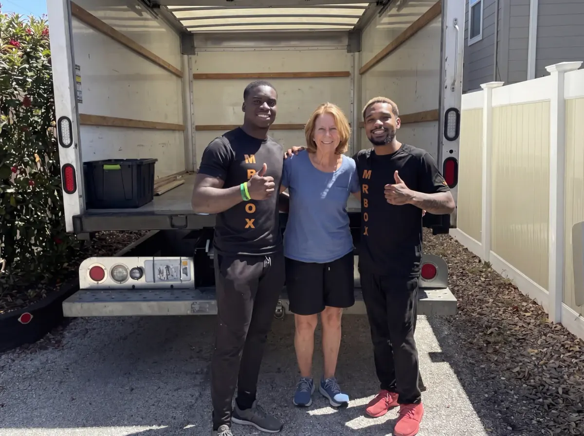 A smiling customer between two movers in front of an open truck