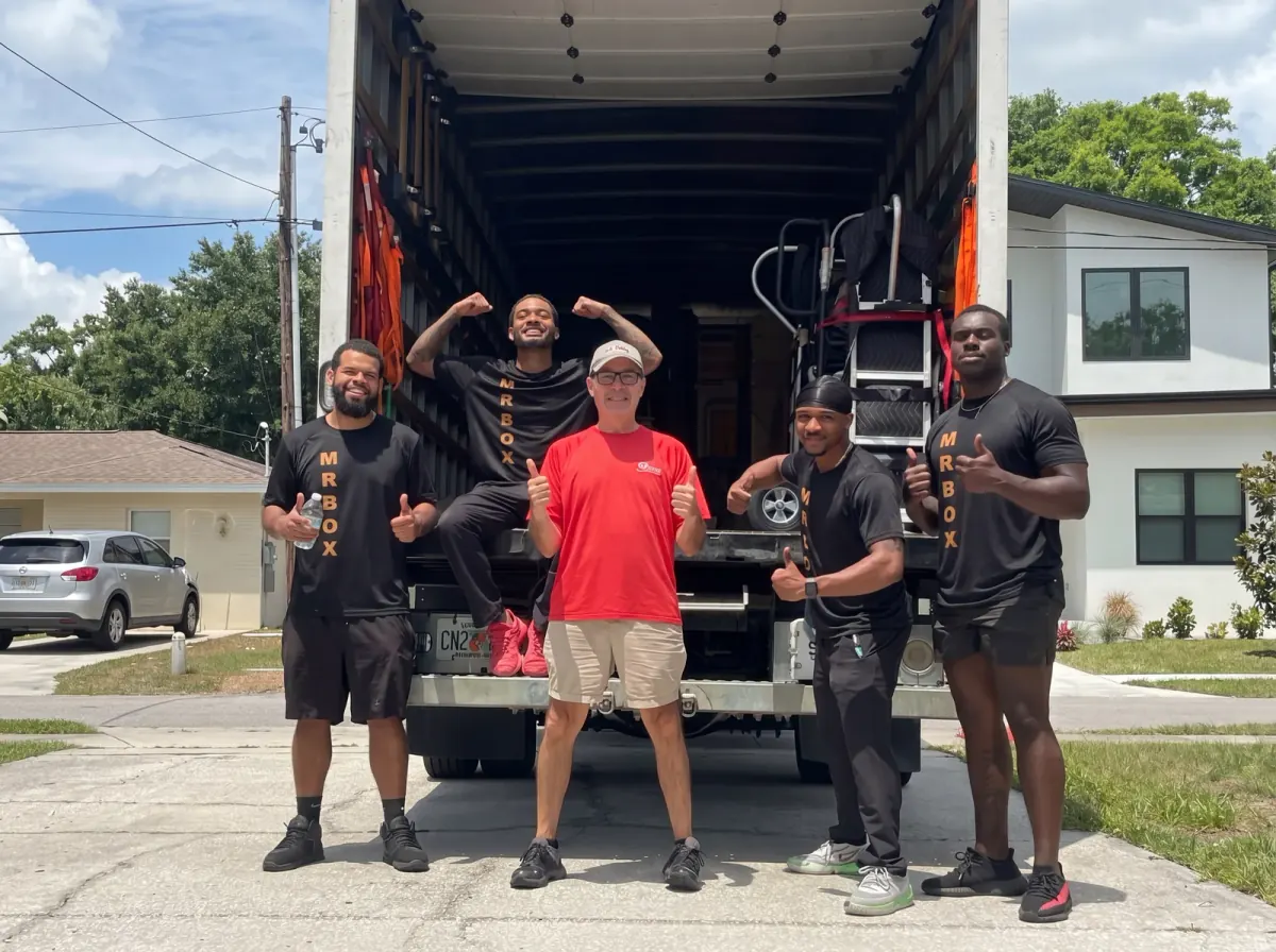 A wider view of a customer in a red shirt and four movers posing at a truck